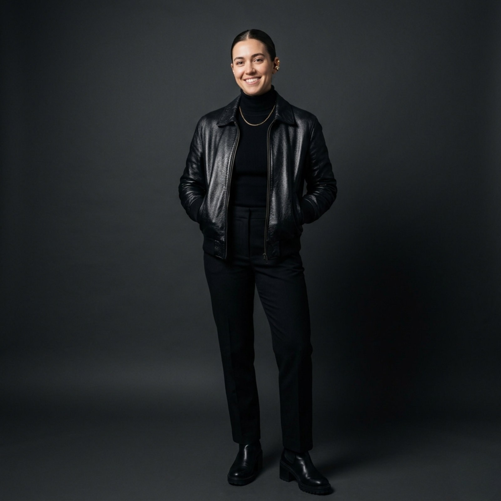 Woman in all-black monochrome outfit: black leather bomber jacket over ribbed turtleneck with tailored black trousers